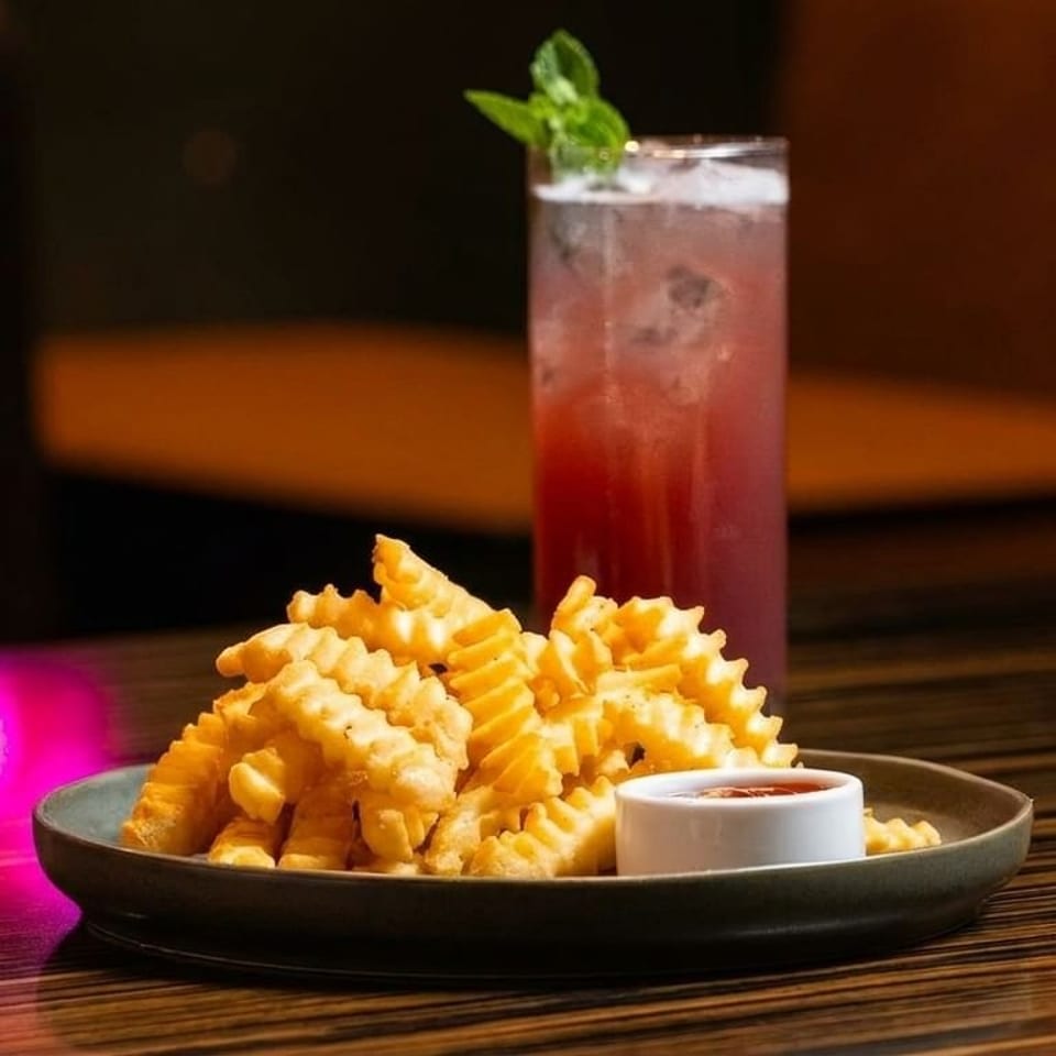 A plate of golden waffle fries with ketchup and a tall glass of red cocktail with mint.