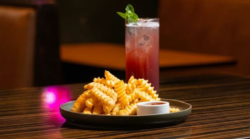 A plate of golden waffle fries with ketchup and a tall glass of red cocktail with mint.