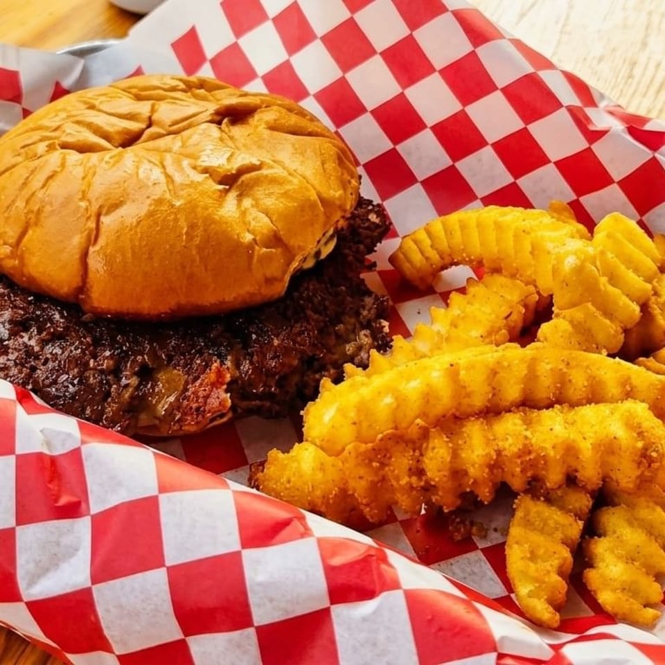 A burger with a thick patty and crinkle-cut fries in a red and white checkered paper-lined basket.