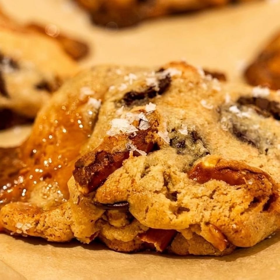 Close-up of a freshly baked chocolate chip cookie with melted caramel and sea salt flakes.