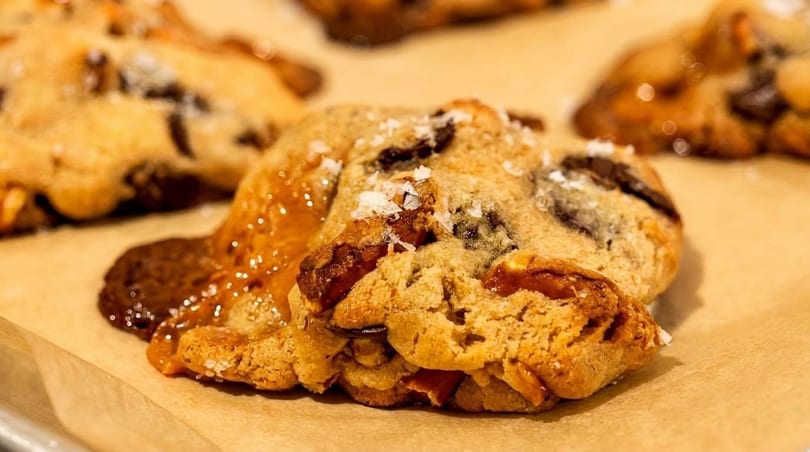 Close-up of a freshly baked chocolate chip cookie with melted caramel and sea salt flakes.